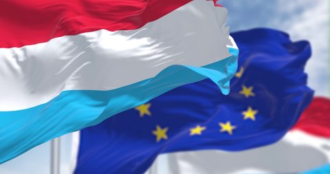 Detail of the national flag of Luxembourg waving in the wind with blurred european union flag in the background on a clear day. Democracy and politics. European country. Selective focus.
