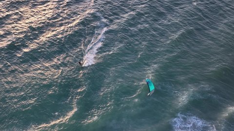 Aerial birdseye view of a kite surfer at sunset sailing over cresting white waves with beautiful sunlight softly reflected off the water