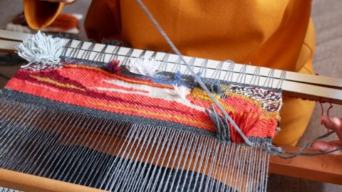 Artisan is weaving and cutting the ends of the threads to create a cut pile carpet effect. Making colored tapestry