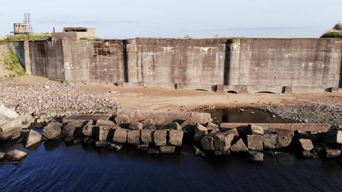 Surrounding wall has collapsed, the sand dam is eroded, and the underground wall of the fortification structure is visible. Aerial view of ruined fort remains and artificial Obruchev Island