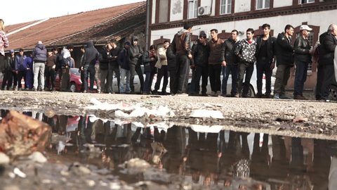 Refugees are standing in line for food in a temporary refugee camp. the camera is placed on the ground, showing the reflected image on a water puddle. Feb 22nd, 2017, Belgrade, Serbia.