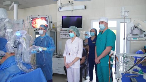 KYIV, UKRAINE - August 2021: Da Vinci robot operating the patient. Lots of medical workers came to watch the robotic equipment at work. Modern well-equipped surgery room at backdrop.