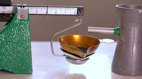 Using powder measure to trickle gunpowder onto weight scale and hand removing trickler plus gunpowder when amount is correct - Static closeup of home reloading of ammunition process