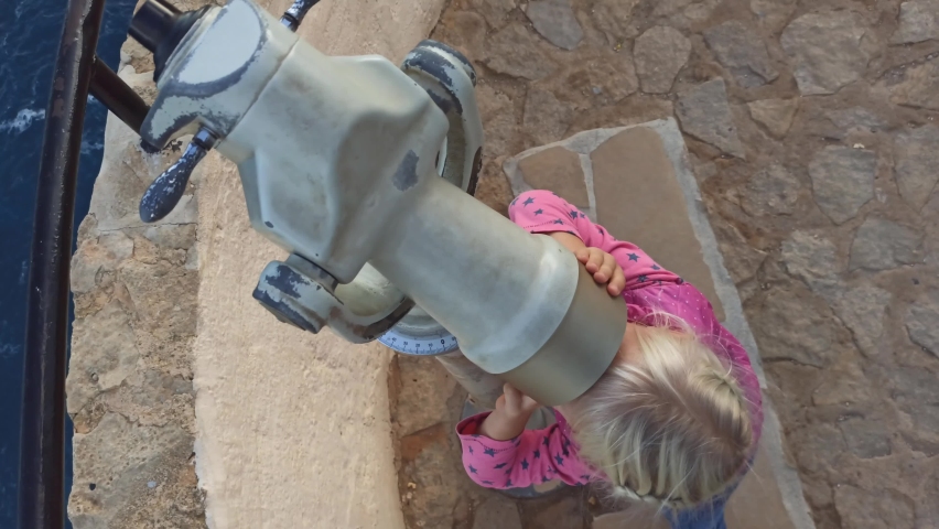 Little blonde girl having fun looking from the other side through a telescope. High angle view