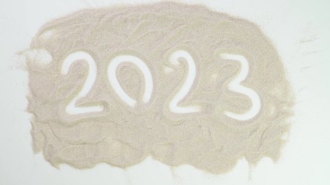 2023. Top view draw on the sand. Caucasian hands write text in beige sand. Vacation and travel. Beach on vacation. Sand painting. Creativity from natural materials.