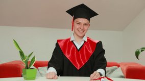 A young university graduate student expressing joy and excitement to celebrate his achievement of degree graduation holds a scroll with a red satin ribbon in his hand