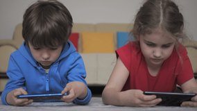 Children Playing Games In Phone at Home Lying on Floor. Kids Playing Video Game on Mobile Phone. Boy and Girl Plays Video Game Smartphone. Friends Using Phone for Gaming Online Education Social Media.
