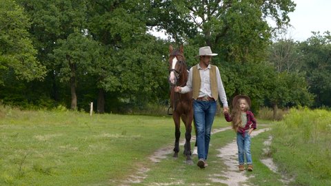 Cowboy with his daughter walking with a horse on a forest road. Happy cowboy family. Slow motion.