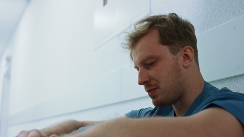 Crying depressed doctor sitting corridor after bad day close up. Portrait of stressed man medic experiencing hard emotions on clinic floor. Emotional sad medicine worker resting in hospital hallway. Royalty-Free Stock Footage #1090115727