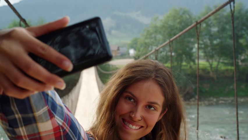 Beautiful woman taking photo selfie using phone at mountain nature landscape. Portrait of hitchhiker posing camera on mobile device outside. Happy girl relaxing enjoying active leisure. Travel concept