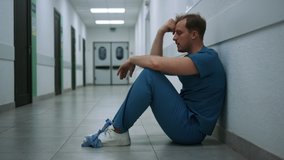 Stressed surgeon staying in empty clinic hallway after hard operation. Depressed doctor sitting alone on floor hospital corridor. Unhappy man physician throwing medical gloves holding hand on face. - Powered by Shutterstock - Get 15% off with code: PIKWIZARD15