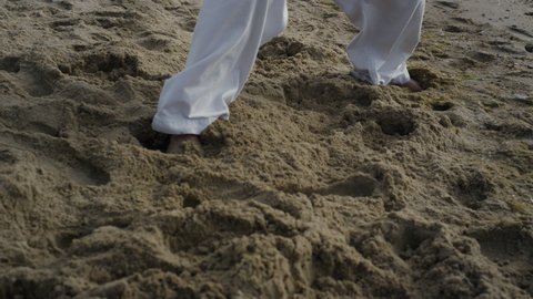 Bare man legs standing beach sand in karate position close up. Unknown sportsman feet training fighting exercises outdoors cloudy day. Strong athlete workout martial arts on seacoast summer morning.