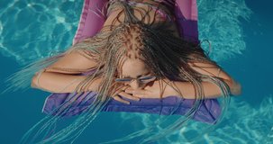 View from above: A child with afro pigtails swims on an inflatable mattress in the pool. 4k video
