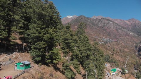 Drone flying over mountain in Tosh valley showing pine trees, village in mountains.
Snow covered Himalayan range in far distance