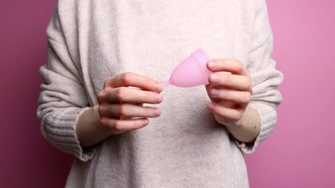 An unrecognizable woman in a sweater demonstrates a pink menstrual cup.