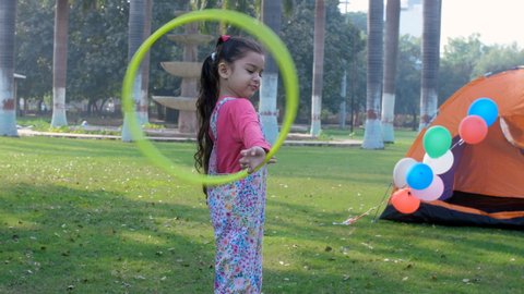 A happy schoolgirl twisting and turning a yellow Hula hoop in her hand - playtime, a fun activity, picnic . A sweet little kid playing alone in the public park - leisure time, a city park, an urban.