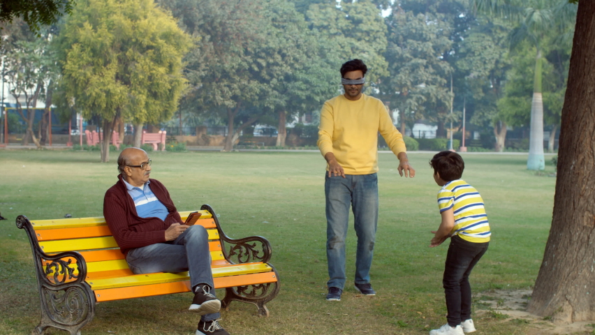 A happy Indian father playing a blindfold game with his son - picnic in a park, blind man