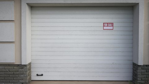 Wide shot white garage door with For sale announcement and no people. Front view real estate property outdoors. Advertising and selling concept