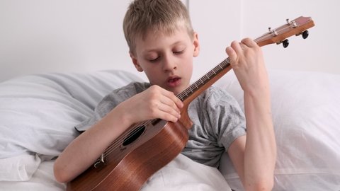 The child plays the ukulele. The boy is practicing to play the guitar. Stringed musical instrument close-up. Music hobby. Ukulele chords. Online education