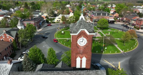 Clock tower reveal of roundabout in small American town. USA flag flies on spring golden hour day. Aerial truck shot.
