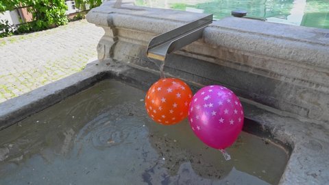 Pink and orange balloon with white stars pattern spinning caused by running water at fountain at the old town of Basel on a sunny spring day. Slow motion movie shot May 11th, 2022, Basel, Switzerland.