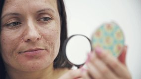 4k video of woman with bad skin looking through magnifying glass and holding mirror.