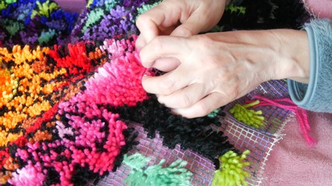 Hand embroidered carpet. A woman using a special hook and thread embroiders a carpet with pink threads. Handmade carpet embroidery. Women's hands create a pattern using multi-colored threads.