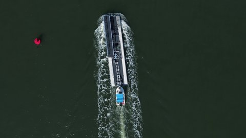 Small boat delivering a large pontoon passes a navigation marker on a river canal. High drone view.