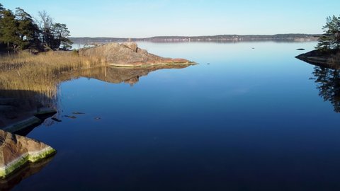 Low forward aerial of cliffs, reeds and still water in eastern Sweden