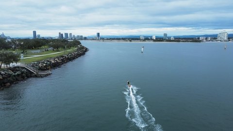 A jet board carves through the glassy waters along a city harbor break wall. Drone view