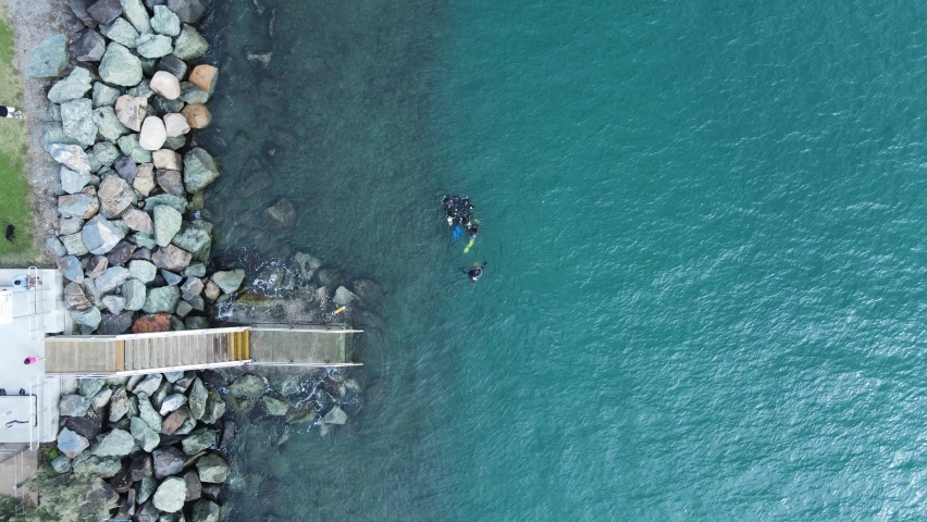 A group of scuba divers gather above the water near a set of stairs leading to the ocean. High drone view | Shutterstock HD Video #1090130521