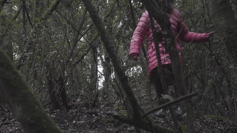 Girl in pink parka walks down steep ravine, then crosses small river