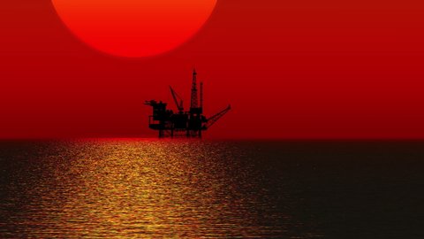 The silhouette of an offshore oil and gas drilling platform over the ocean horizon as the sun sets.