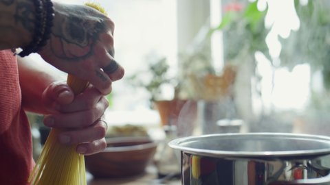Close up shot of hands of chef putting spaghetti into pot with boiling water while cooking pasta