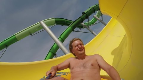 Fun on the water slide at aqua park, close up of young adult man sliding on inflatable ring, lifestyle leisure activity, slow motion