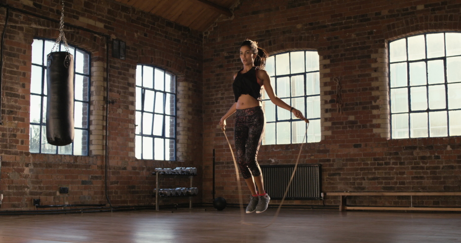 Serious young woman skipping at the gym. Young woman working on her fitness, skipping with a jump rope. Fit hispanic woman doing cardio and skipping at the gym. Woman jumping using a skipping rope Royalty-Free Stock Footage #1090135963