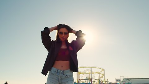 bright stylish brunette in sunglasses in summer on the pier in denim shorts on the Santa Monica pier. A positive sexy girl. Slow motion