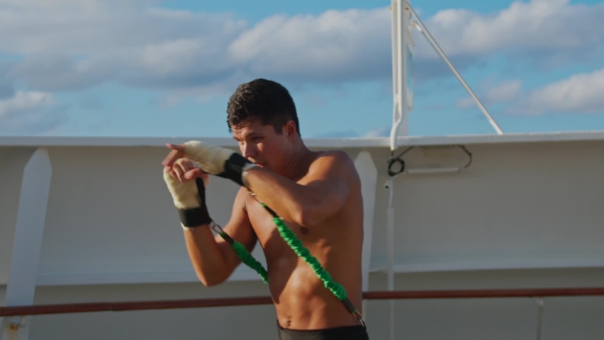 Attractive young man with naked torso does box workout and shadow boxing with resistance band training strap system