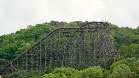 A roller coaster on a forested hill thrills screaming riders at an amusement park