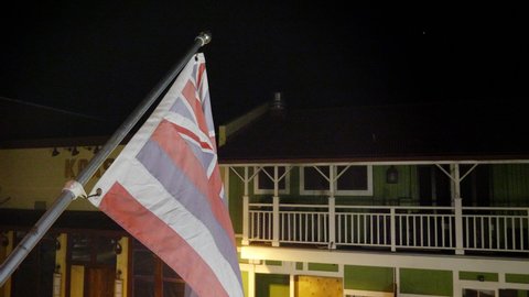 Hawaii state flag on pole in tourist resort waving in gentle breeze at night