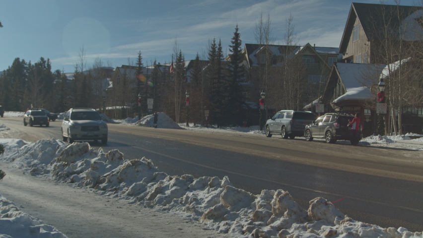 Static view of snow covered white sidewalk and cars passing by in the western state of Colorado, United States on a sunny morning. Beautiful buildings on the side of the road.