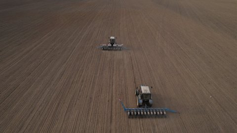 Tractor sowing seed on plowed field. Sowing seeds of corn and sunflower. Blue Tractor with disk harrow on plowing field. Seeding machinery on farm field. Seed sowing in farmland, aerial view.