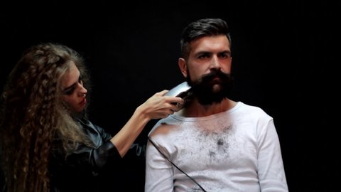 Cutting long beard. Beautiful hairdresser woman doing beardstyle to bearded man in barbershop. Hairdresser makes fun beard style. Barber cutting hair with scissors.