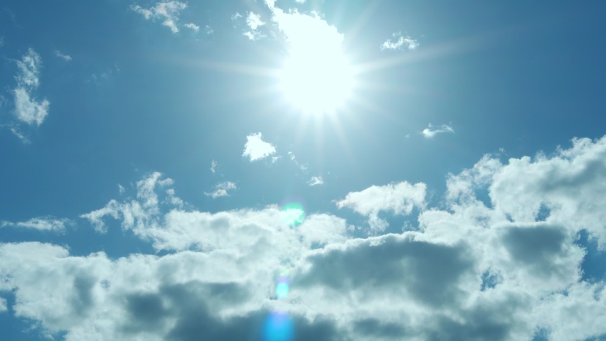 Bright Sun over Soaring White Clouds in Blue Sky, Sunlight, Sun Flare, Rays, Slow Motion, Timelapse. Sky Sun and Clouds on Summer Sunny Day. Relax, Beauty. Clouds Flying towards Sun.