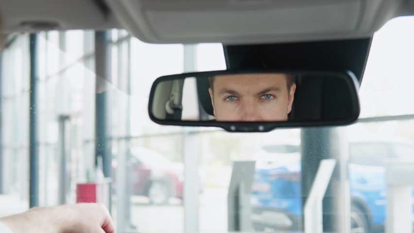 Elegant man looks at the car mirror of his new car in a car dealership