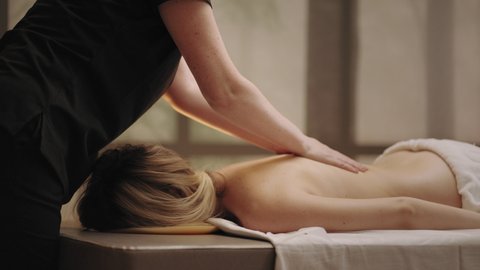 chiropractor is massaging back of young female patient in massage parlor, curing and preventing scoliosis
