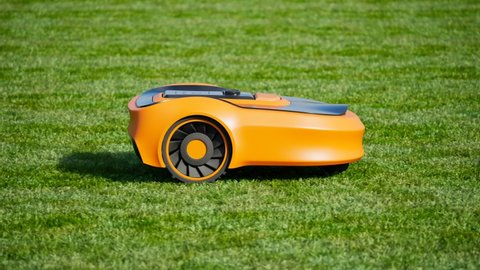 A lawn robot mows the yard. Robotic lawnmower trimming the grass. House yard auto lawn mower cutting grass. Wireless controlled smart equipment for garden grass mow. Modern remote technology.