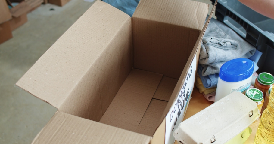 Close up of volunteer putting donated position inside cardboard box for helping people from Ukraine. Charitable foundation for supporting country during war.