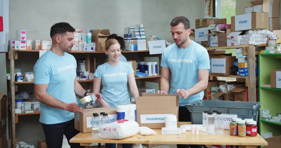 Teamwork of volunteers filling cardboard package with medications while helping in charitable foundation. Concept of people, sincere help and health care. Royalty-Free Stock Footage #1090145171