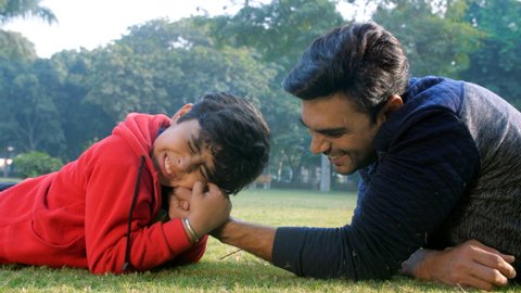 A young Indian boy doing arm-wrestling with his father - picnic, Indian family, physical strength, parenting. An excited little kid playing with his father in a park - father-son bonding, quality time